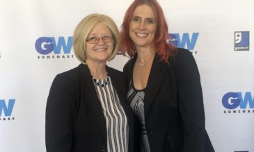 Two women standing in front of a white backdrop covered in blue logos for GW Suncoast and Goodwill.